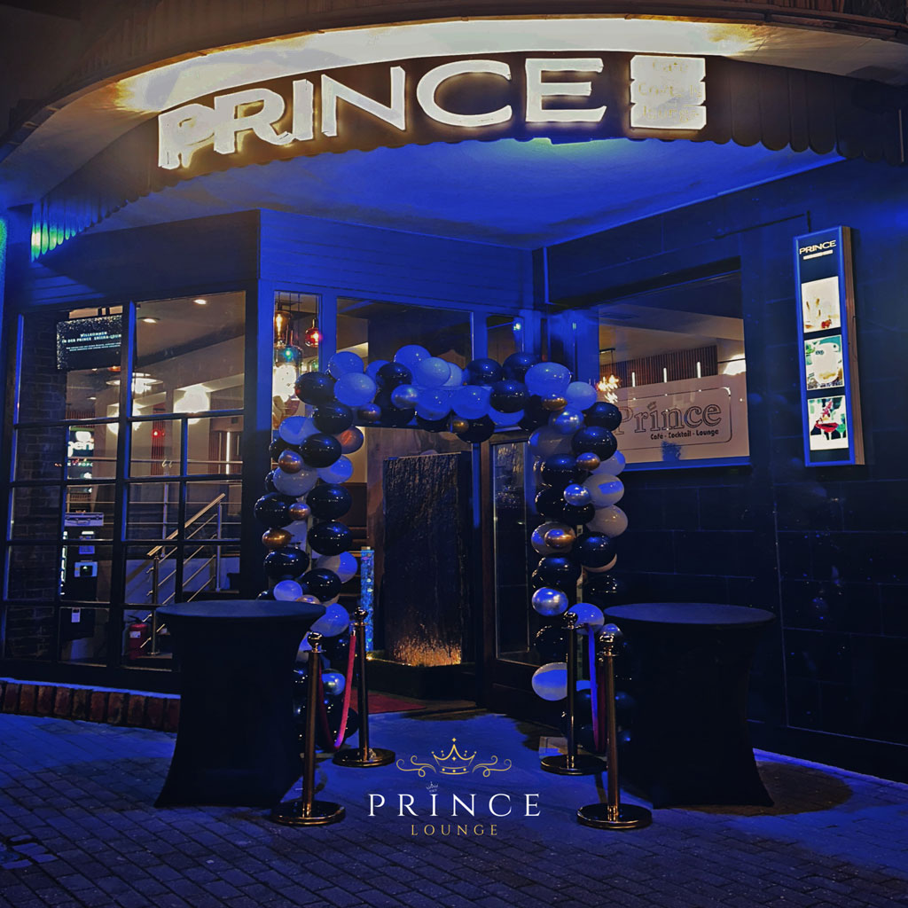 Eingang zur Prince Lounge, dekoriert mit schwarzen und weißen Luftballons, abends beleuchtet.