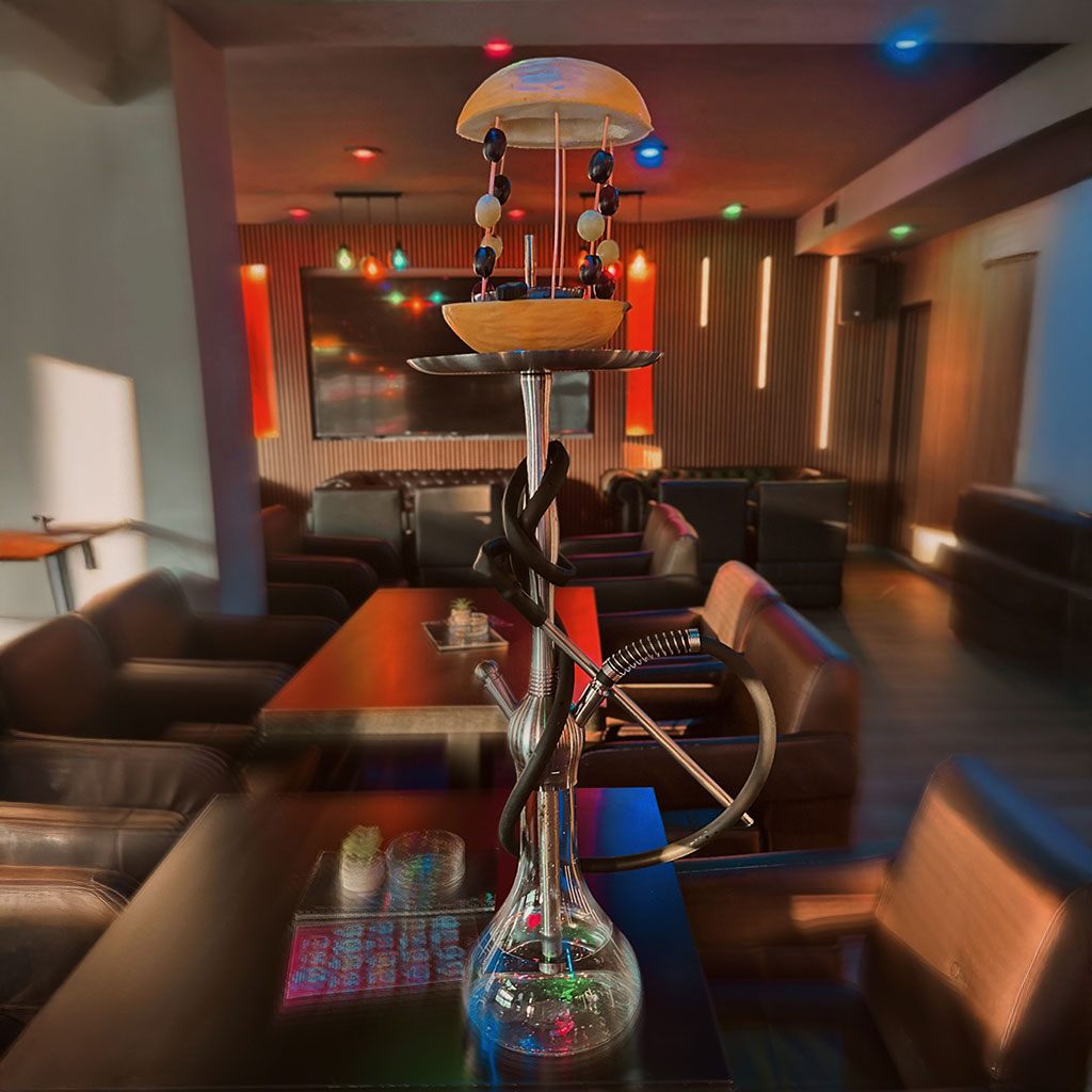 Eine stilvolle Wasserpfeife in einer modernen Lounge mit bunten Lichtern und gemusterten Wänden.